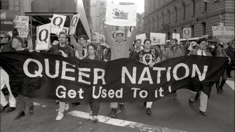 A photo of a march with Queer Nation activists holding a banner saying "Queer Nation: Get Used To It!"